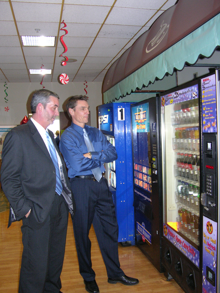 Colin Walsh, right, marketing director for Hometown/Tri-City Vending, came up with the idea of turning a glass front soda machine into a &lsquo;New Age Bevmart.&rsquo; &ldquo;My idea was to mirror what&rsquo;s happening in c-stores,&rdquo; said Walsh. With that in mind, Ken Martin, left, manager of the Peru location, has route drivers fill the machines with enhanced waters, milk, a few varieties of energy drinks and other beverages as well as soda.