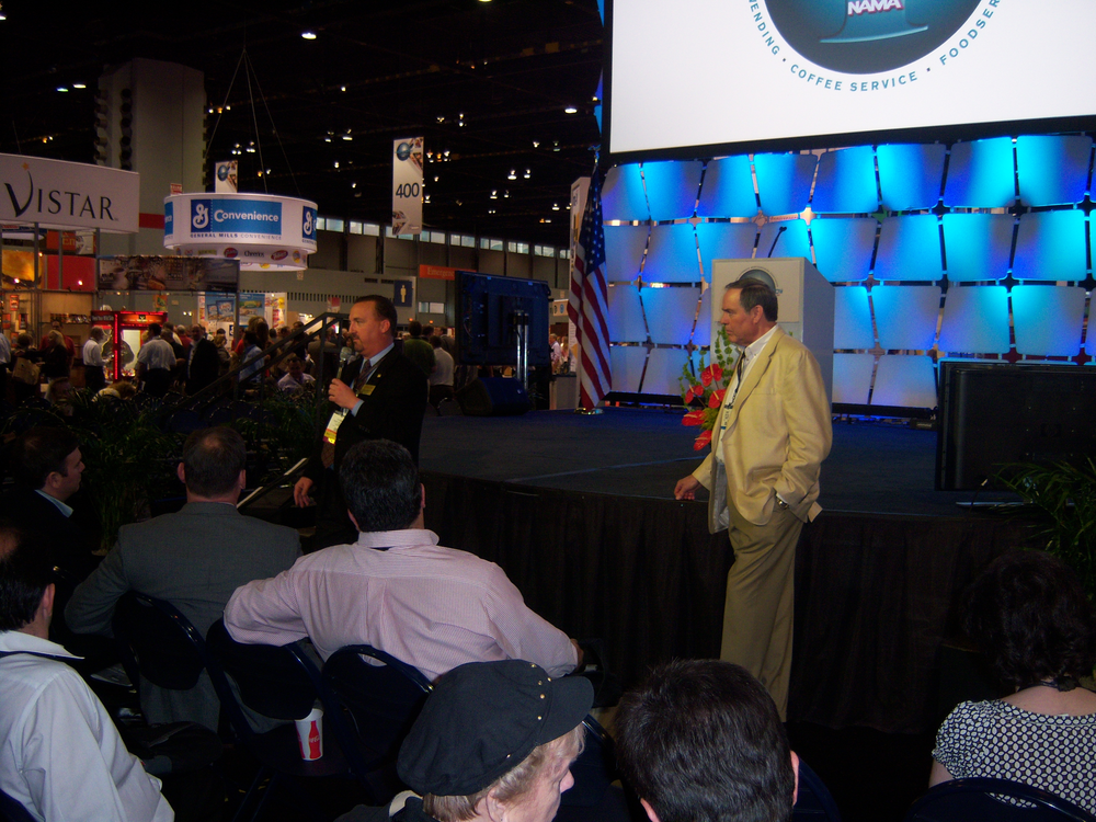 Richard Harvey of A&R Services LLC, Monument, Colo., left, and Jeff Rank, Sterling Services, Canton, Mich., discuss the Avanti Markets and Retail 365 self checkout markets, respectively, during an operator perspectives session at the OneShow trade show.