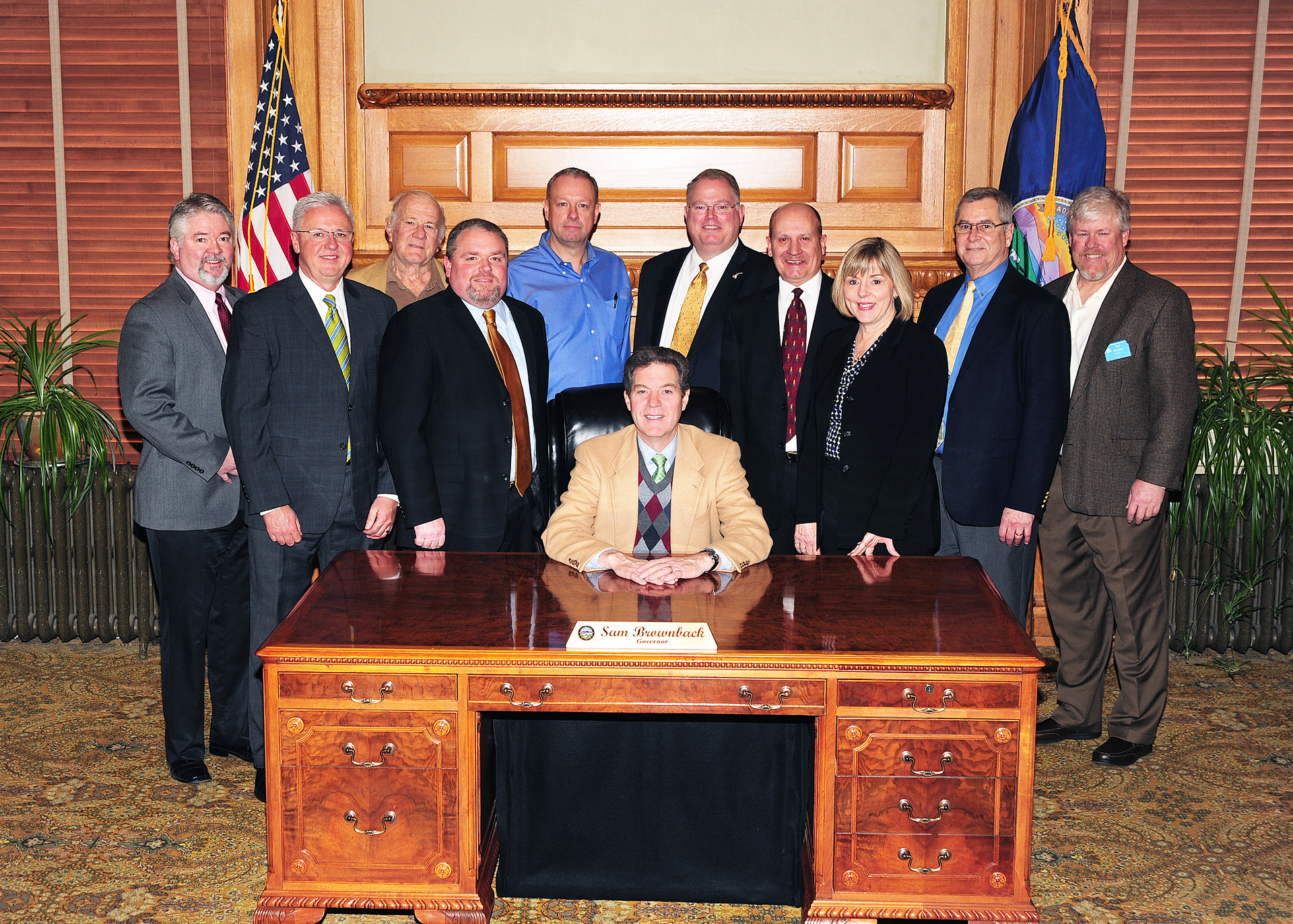 Kansas Governor Sam Brownback (center), surrounded by Mike Cox, John Barnes, Denny Burgess, Chip Stephenson, Joe Hemmelgarn, Claude Bockhold, Bill Bradford, Sandy Larson, Keith Bottorff and Tom Burgess.