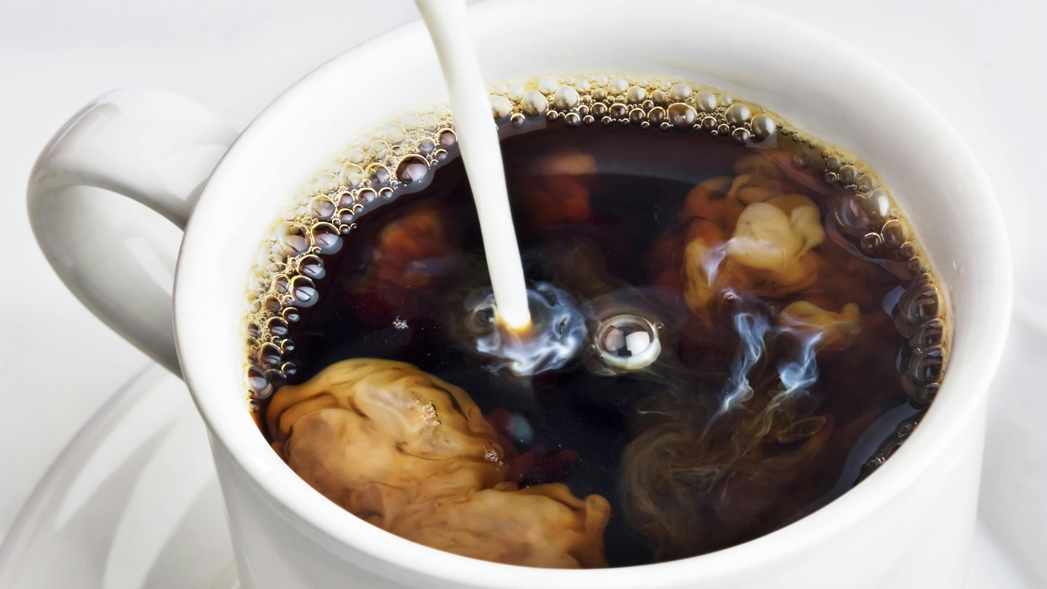 cup of coffee with cream pouring in