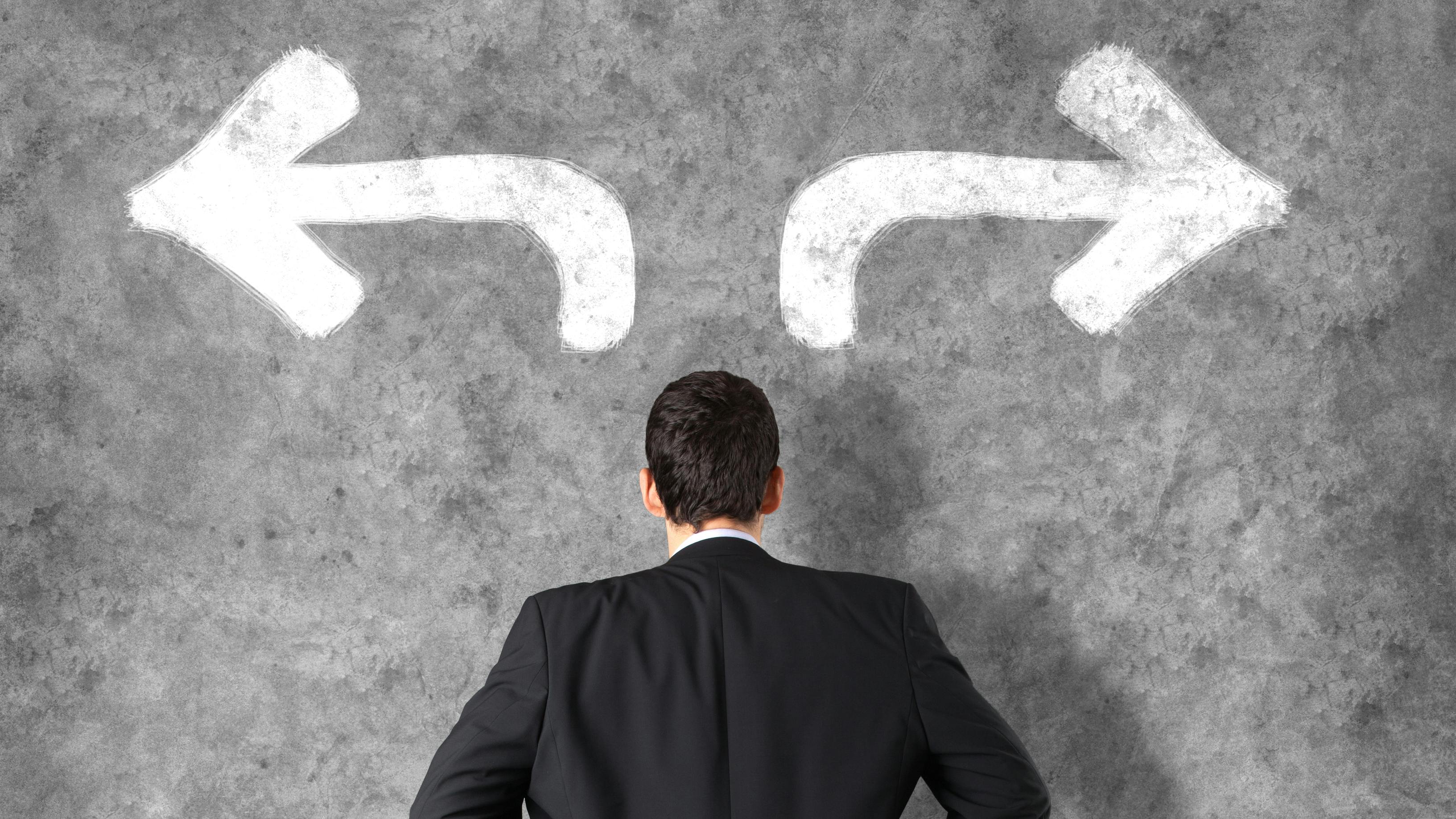 business man looking at two arrows going in different directions