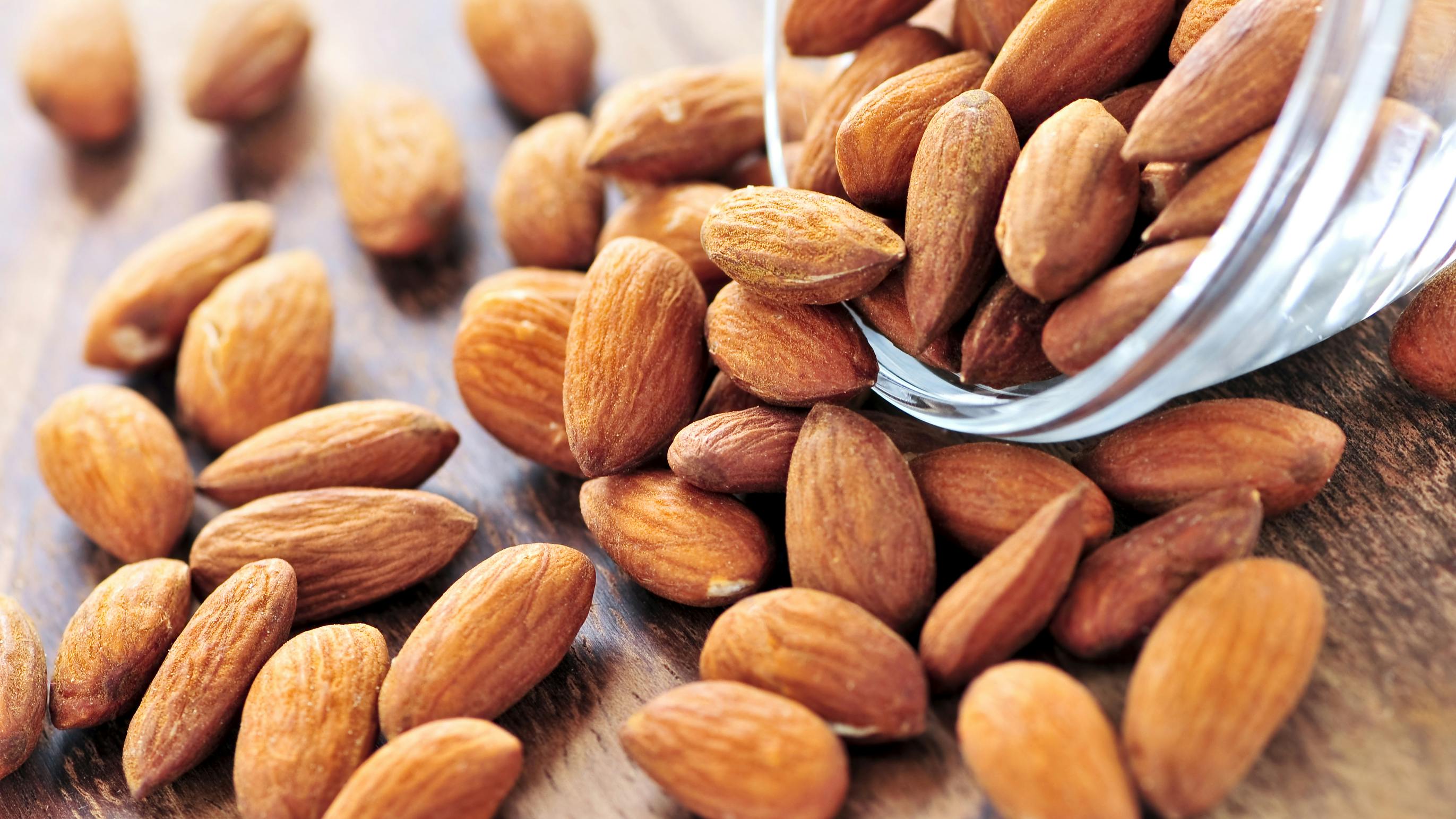 Raw almonds spilling out of small glass bowl
